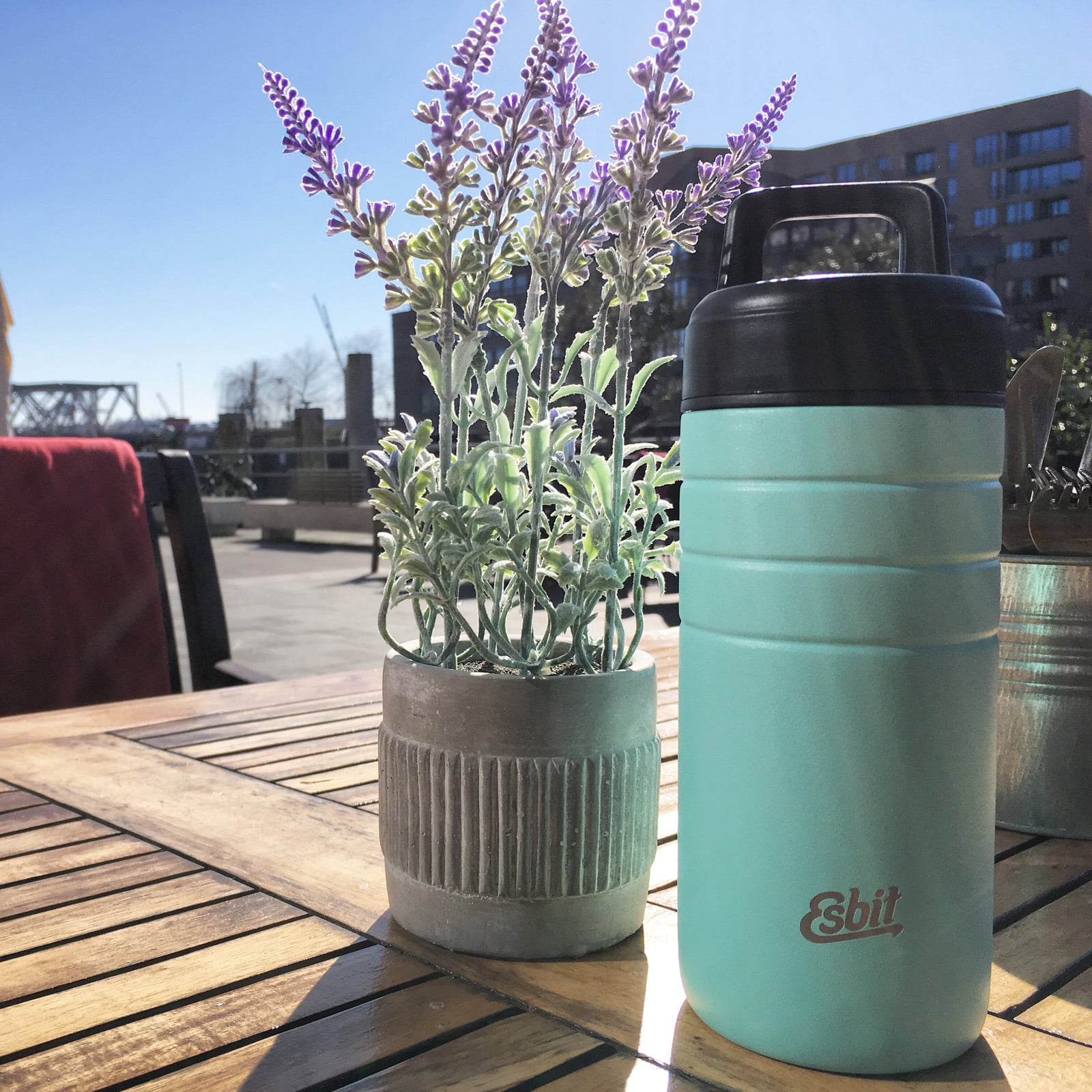Mintgrønt termokrus på et træbord på en terrasse ved siden af en krukke med lavendel
