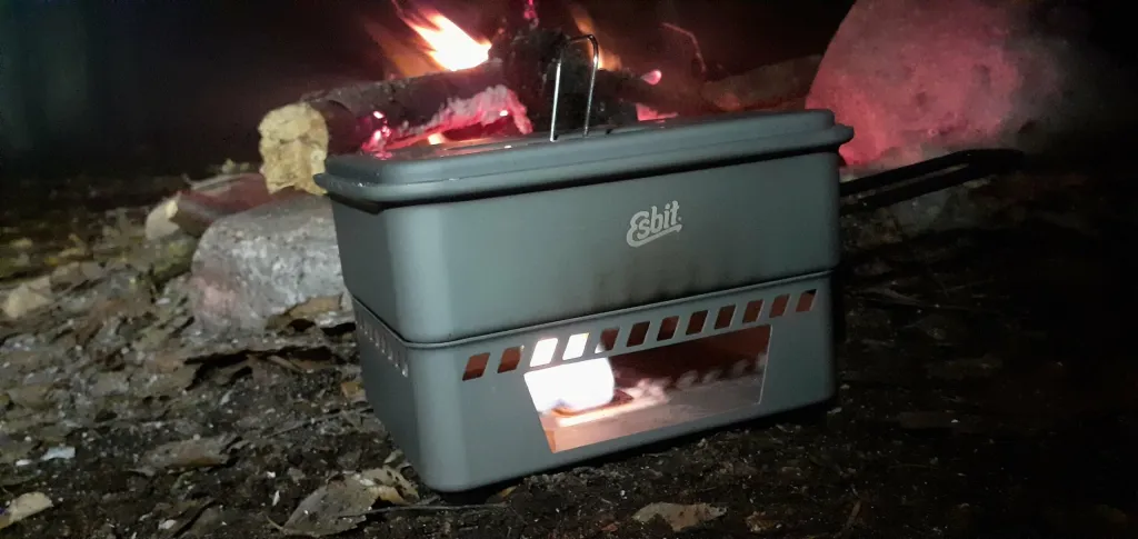Esbit kogesæt med fast brændsel i brug til udendørs madlavning foran et bål i mørket