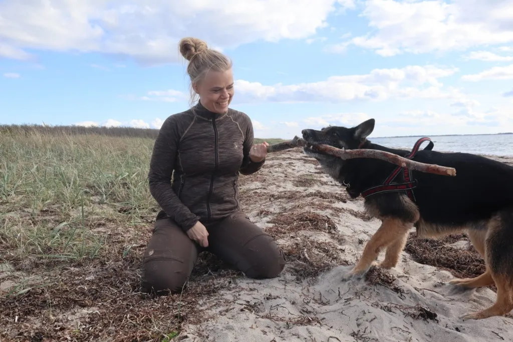Dame iført Deerhunter Insulated Fleece på en strand, hvor hun leger med sin hund