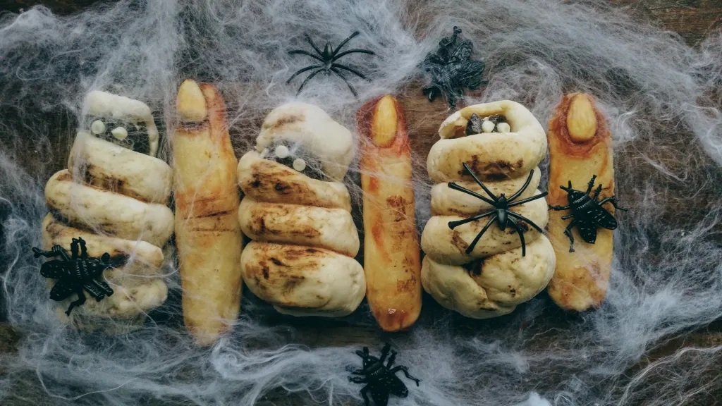 Sjove grillsnacks lavet som heksefingre og mumie-pølsehorn ses med falske edderkopper af plast og edderkoppespind