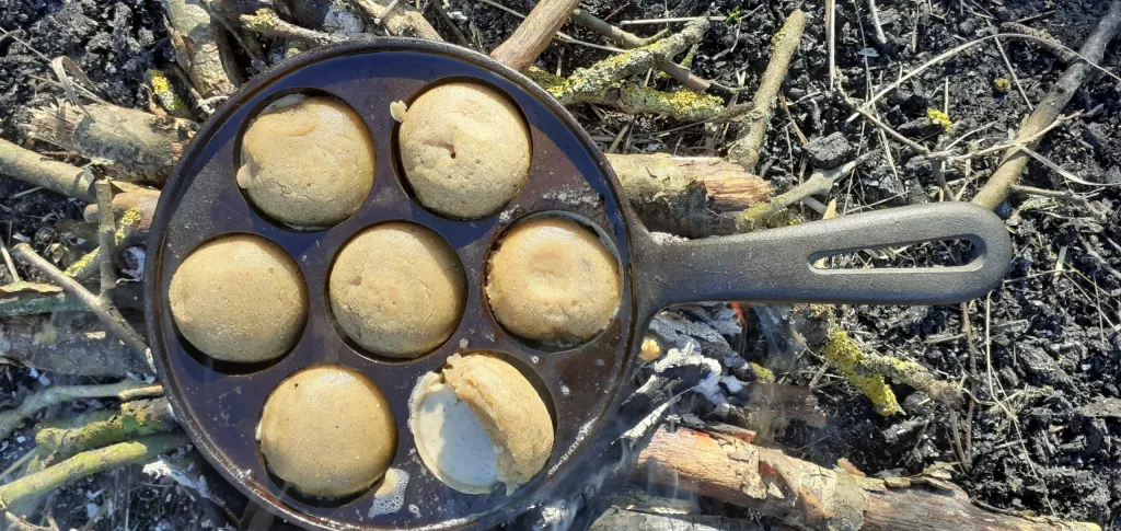 Pandekagekugler tilbederes i en æbleskivepande af støbejern i et bål