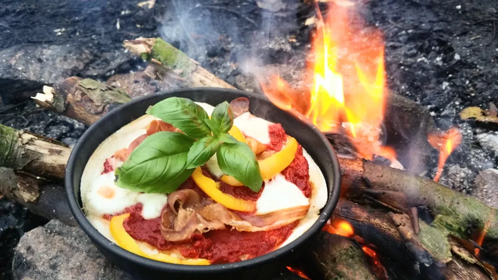 Hjemmelavet pizza med tomatsovs og friske toppings tilberedes på en mini trangia over bål